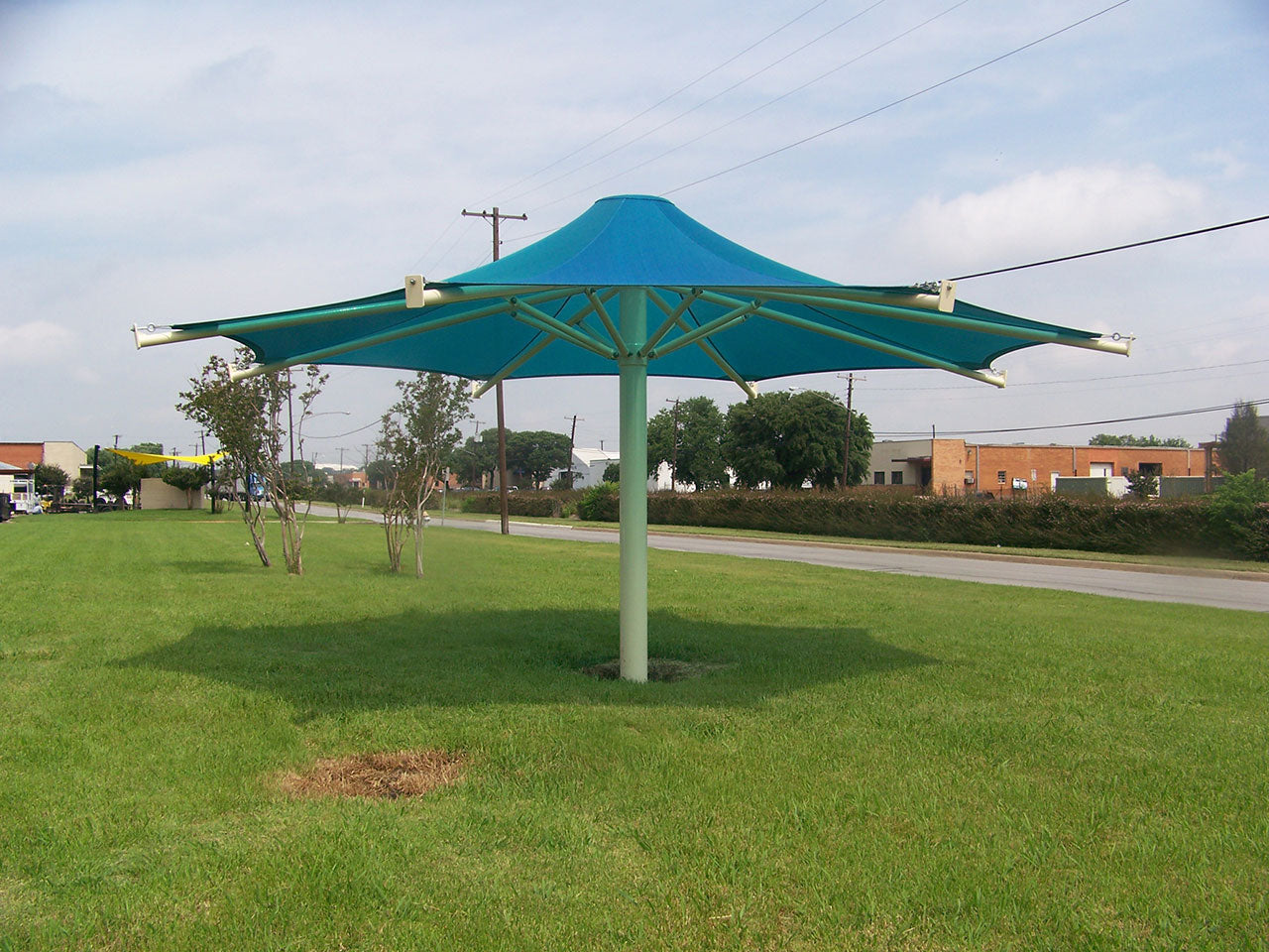 Blue eight-point shade canopy with a single central column on grassy outdoor area, modern umbrella-style structure