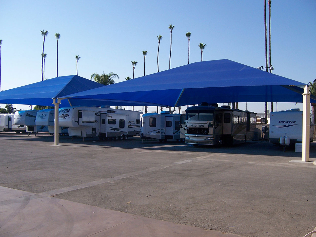 Hip Roof Shade Structure with 4 posts and blue fabric canopy providing UV protection over parked RVs and trailers