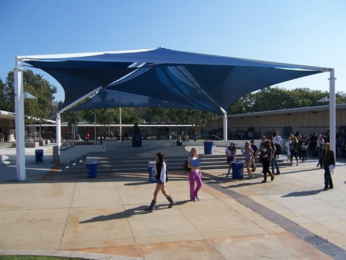 Large blue multi-layer fabric shade structure with steel frame over outdoor school courtyard with students walking beneath