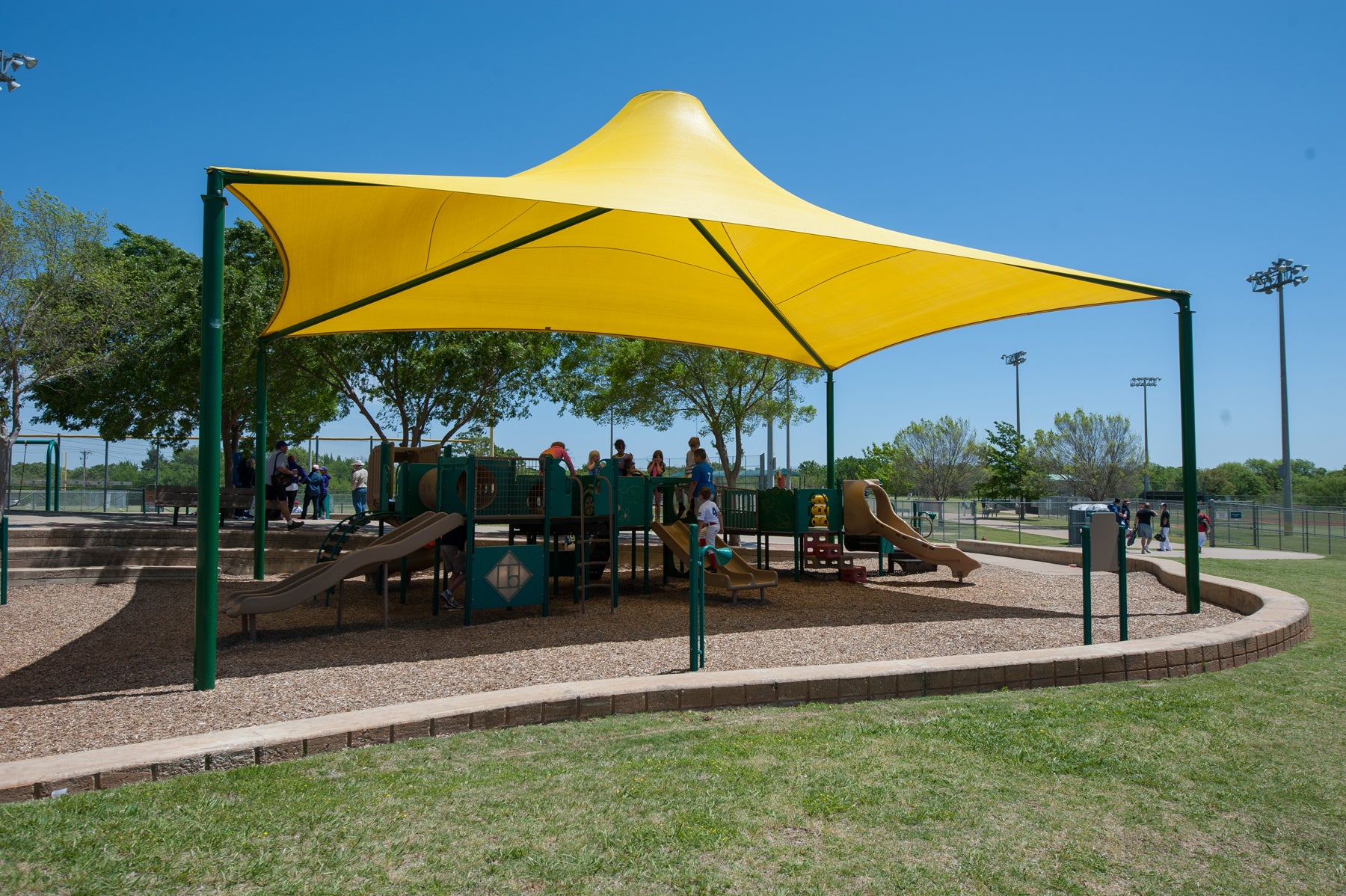 Sahara Roof Shade Structure with 4 Posts in bright yellow, conical design shading playground equipment in sunny park setting