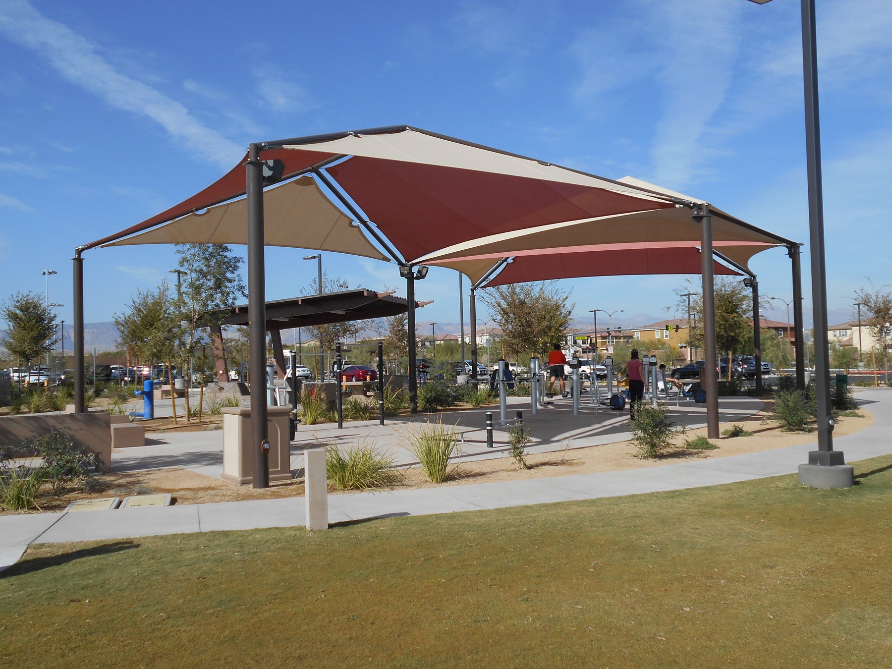 Hip Multi-Panel Shade Structure with four red and beige fabric panels over outdoor fitness equipment in park setting