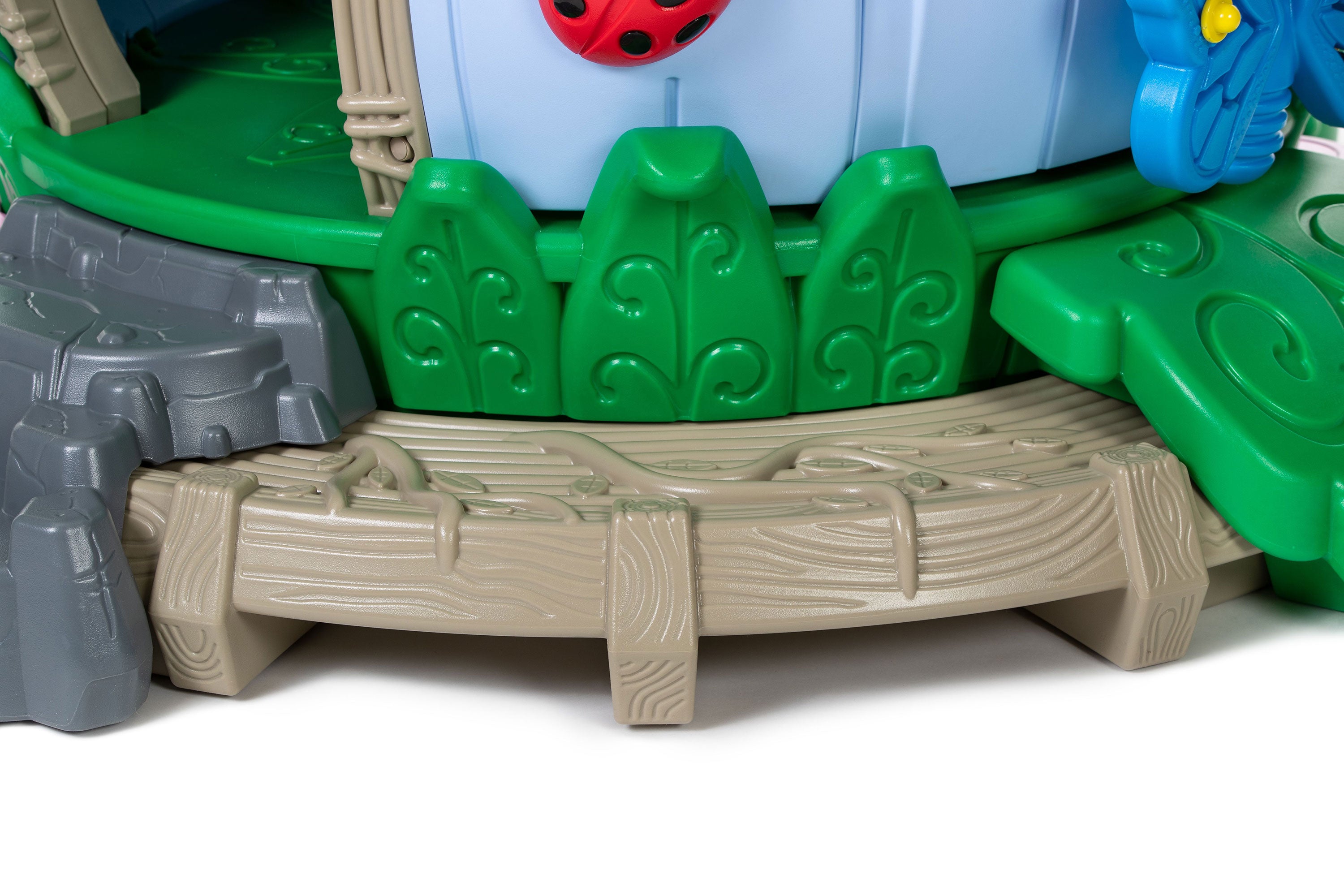 Nature-themed preschool playground with faux log step, green leaf panels, gray rock accents, and a ladybug detail.