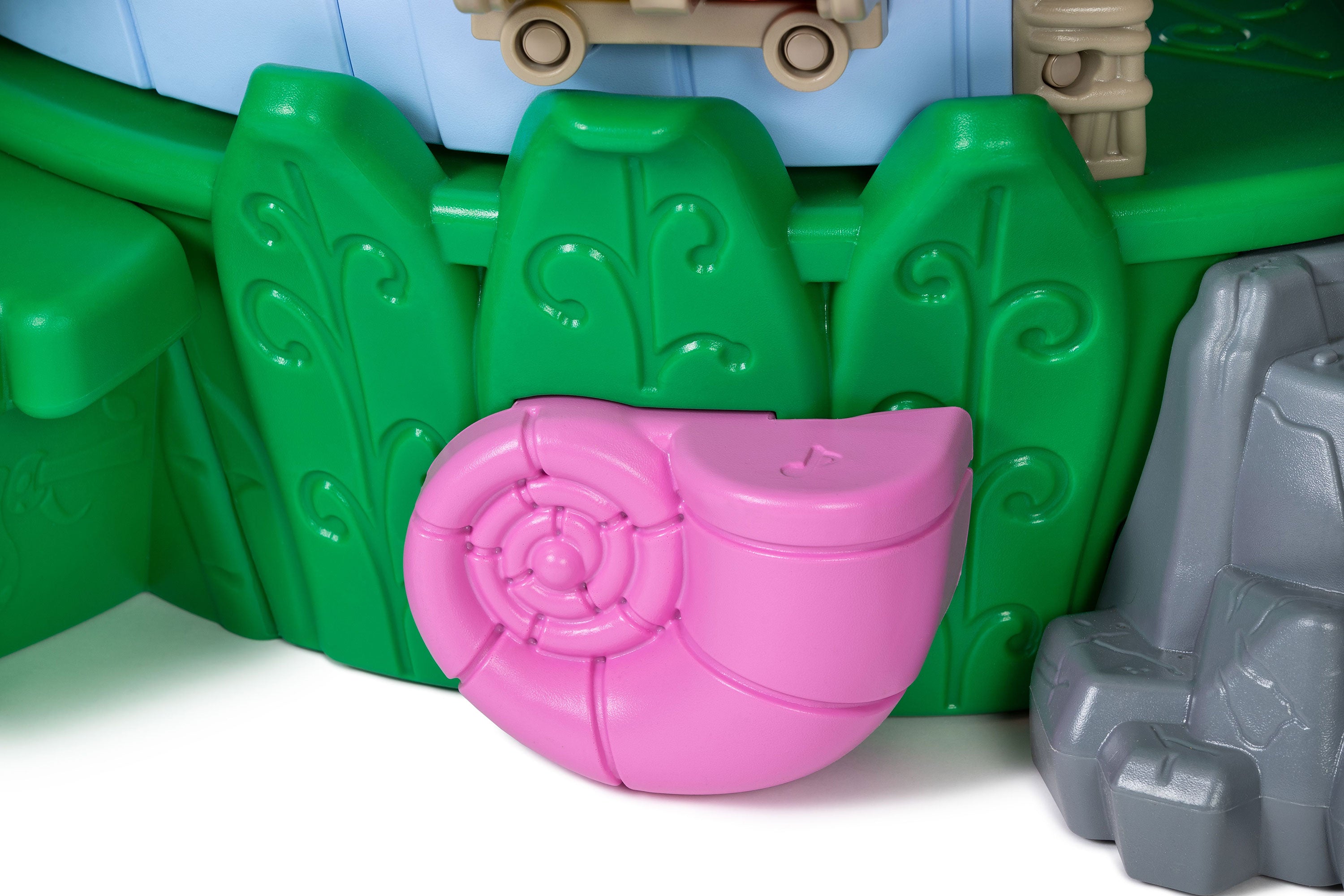 Nature-themed preschool playground with pink snail shell climber, green leaf panels, and gray rock base.