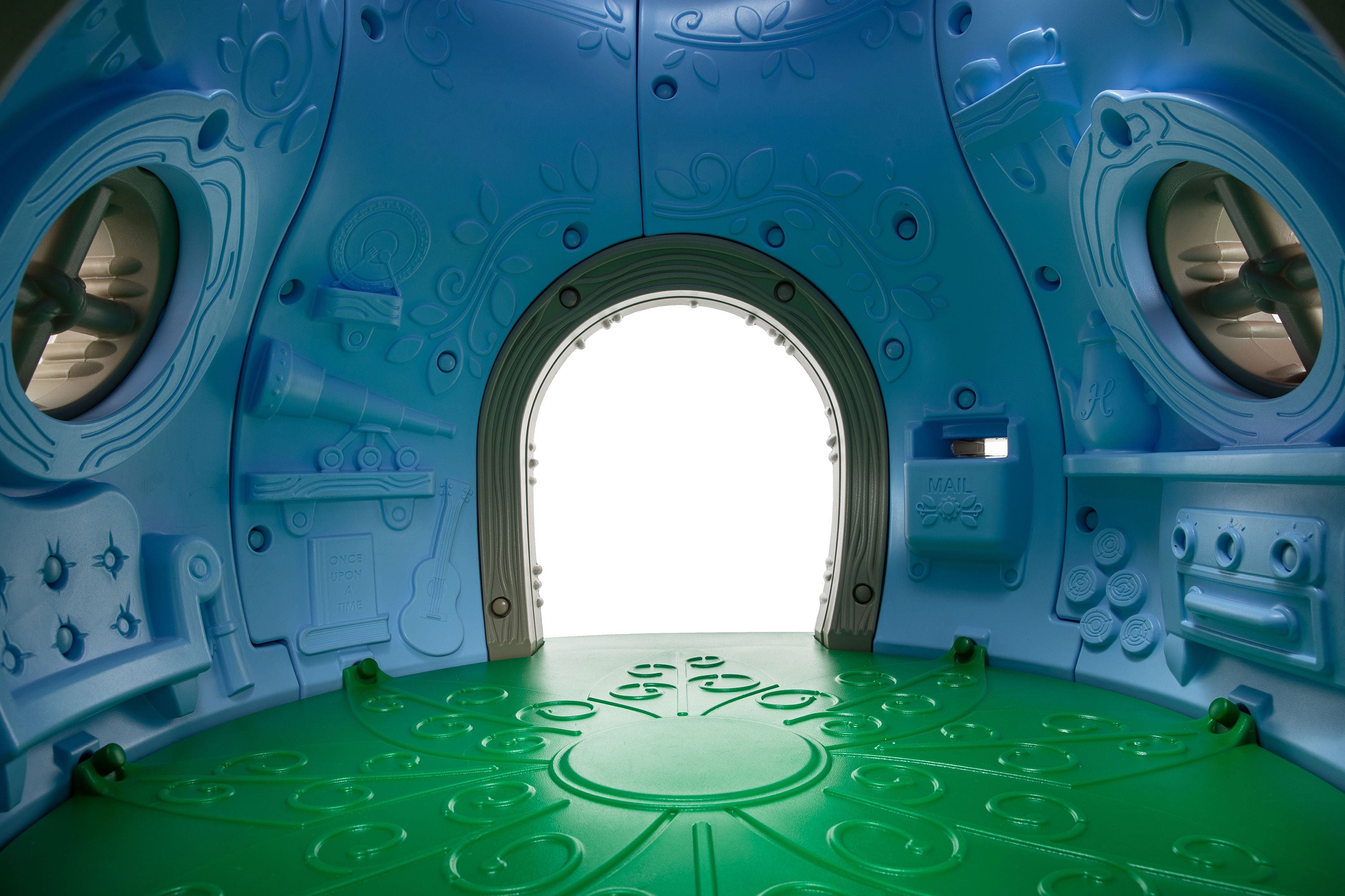 Indoor toddler playground playhouse with leaf-pattern floor, porthole windows, mail slot, stove, and storybook panels.
