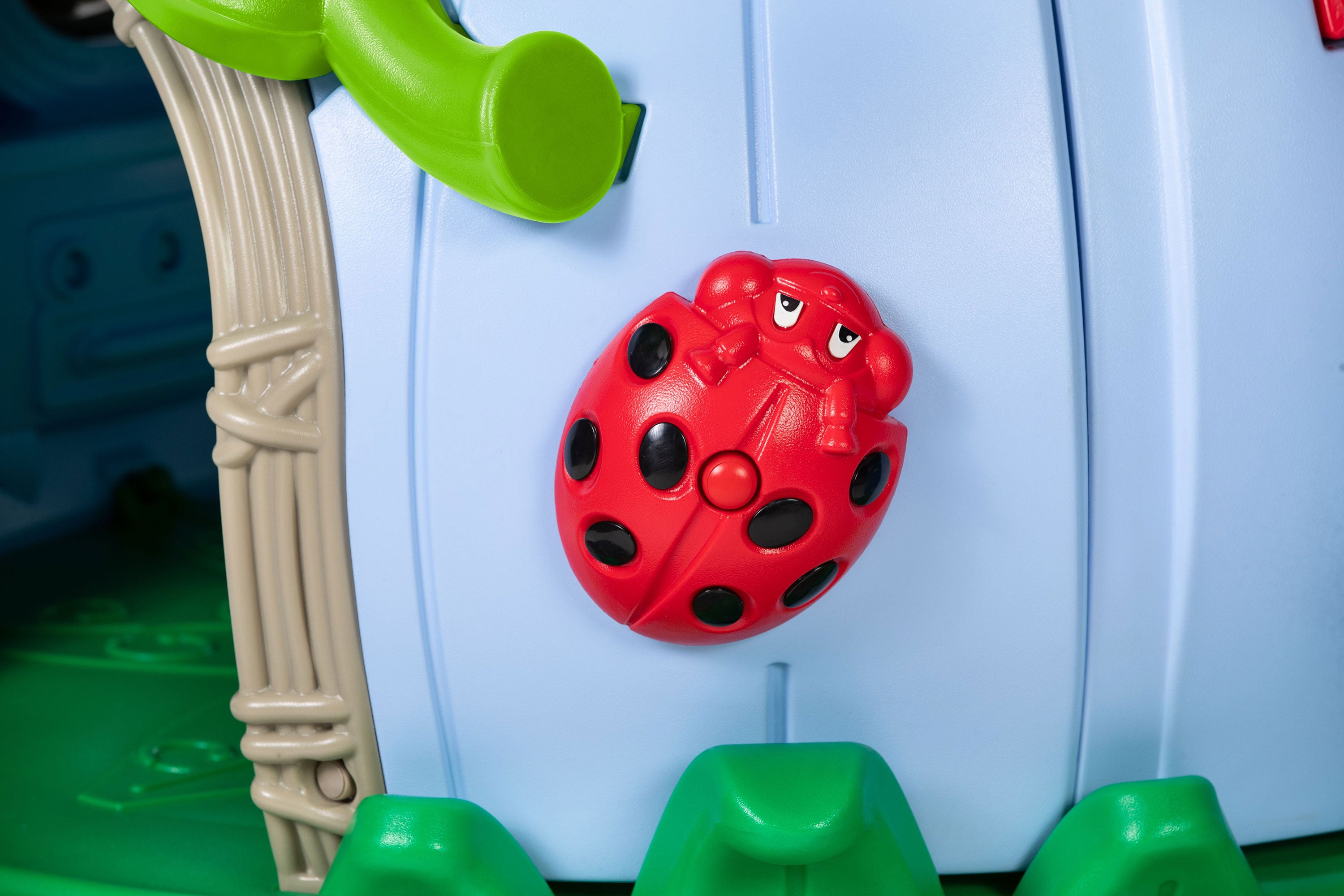 Preschool playground activity panel with red ladybug knob, light blue wall, green step features, and wood‑look trim