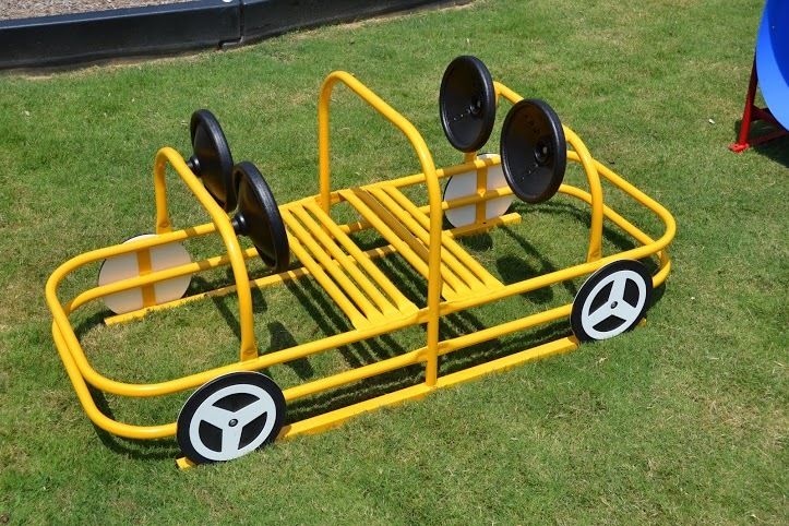 Passenger Car small play equipment with yellow metal frame, bench seating, steering wheels, and wheel-shaped accents on grass