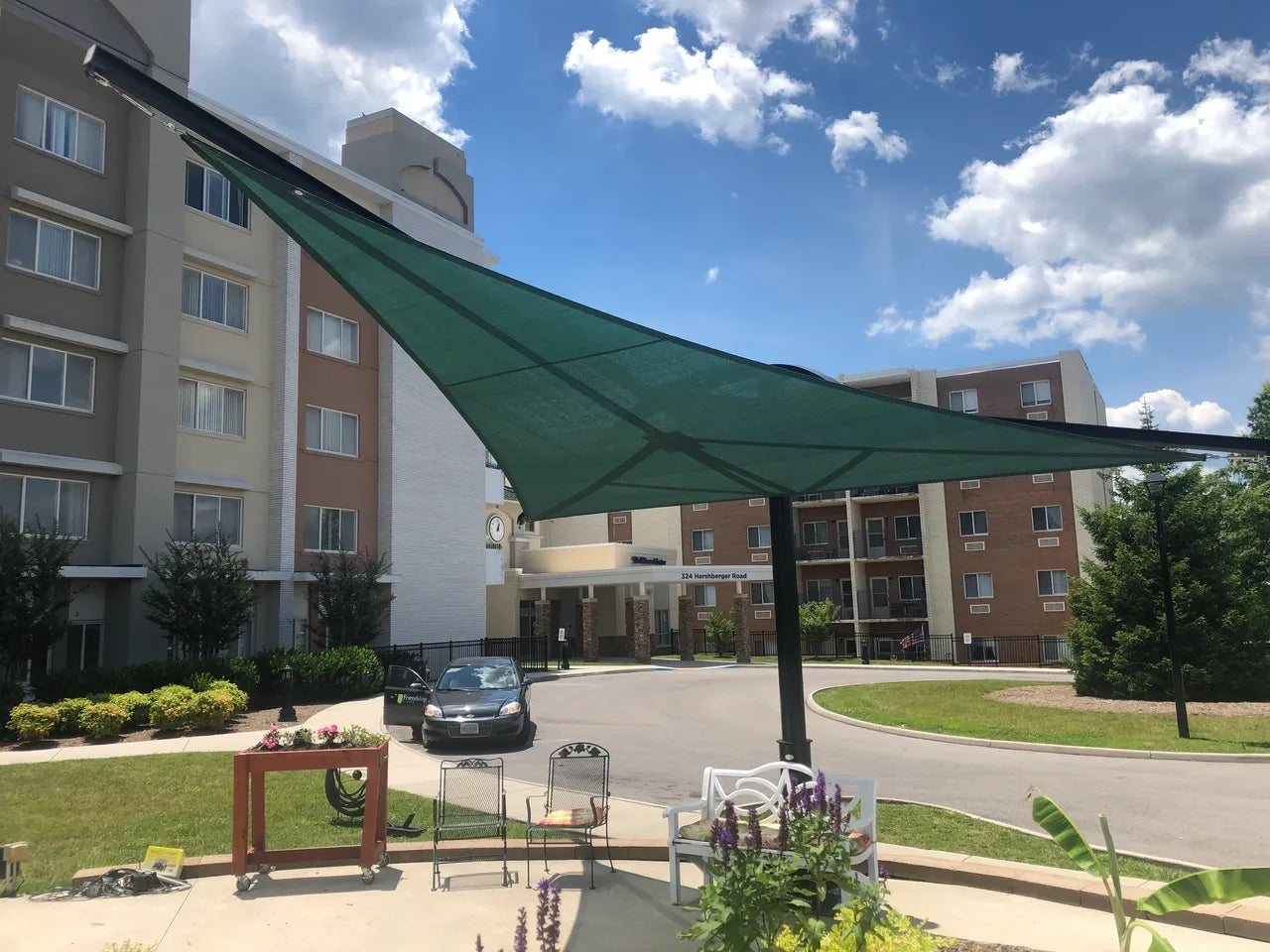 Outdoor patio with rotating triangular shade sail supported by black steel post over seating and garden plants under clear blue sky