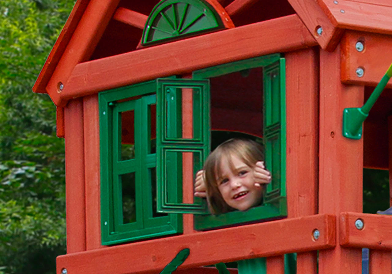 Child peeking through green working shutters of redwood clubhouse with wood roof and decorative dormer on wooden swing set