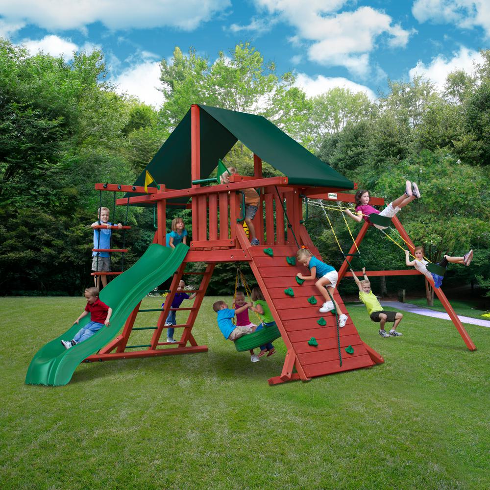 Redwood-finished wooden swing set with green Sunbrella canopy, Alpine Wave slide, rock climbing wall, rope ladder, tire swing, and belt swings with children playing