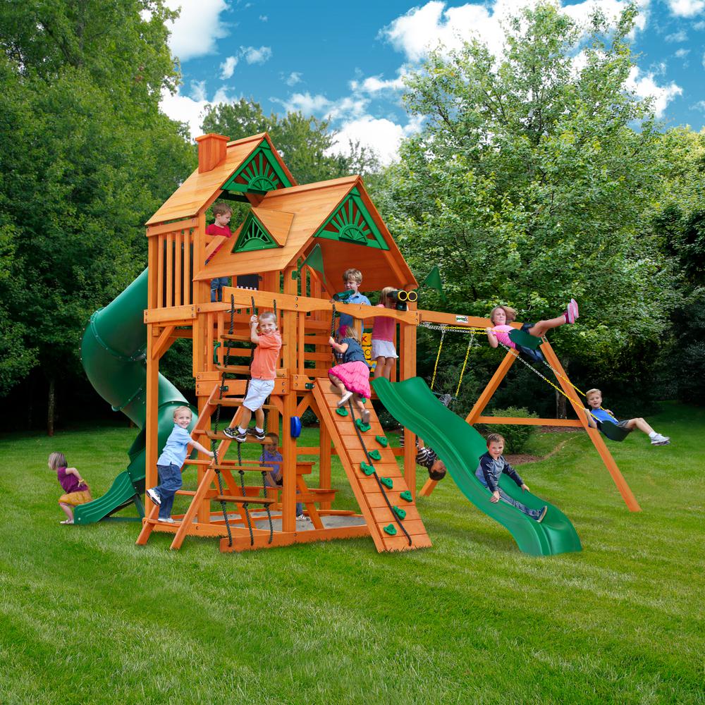 Cedar wooden playset with dual belt swings, climbing wall, green slides, rope ladder, and wood roof with sunburst details