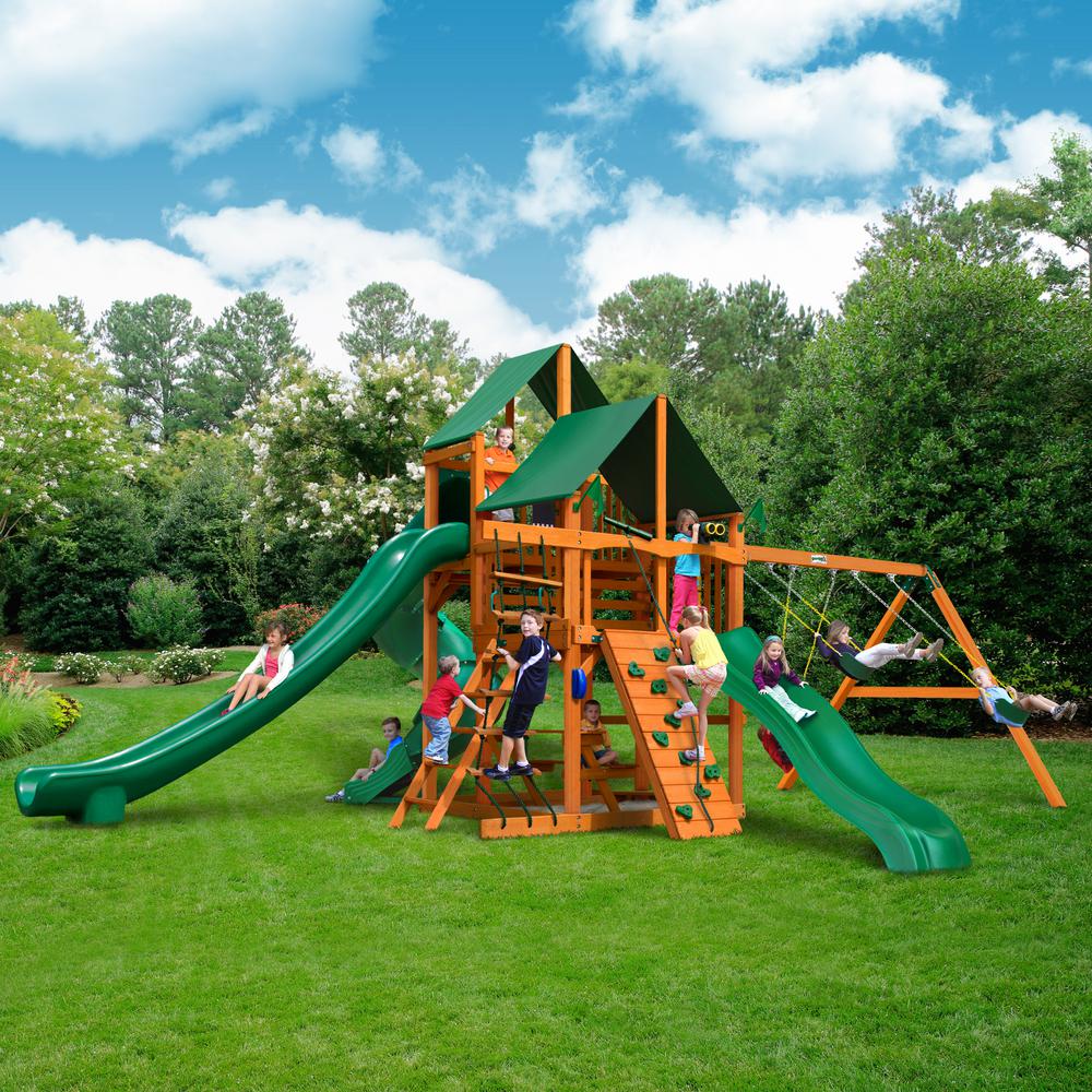 Wooden playset with green slides, swings, climbing wall, and canopy roofs, children playing outdoors