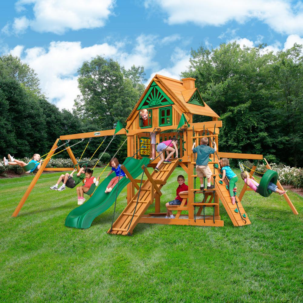 Cedar wooden playset with green slide, climbing wall, tire swing, belt swings, and kids playing on grass