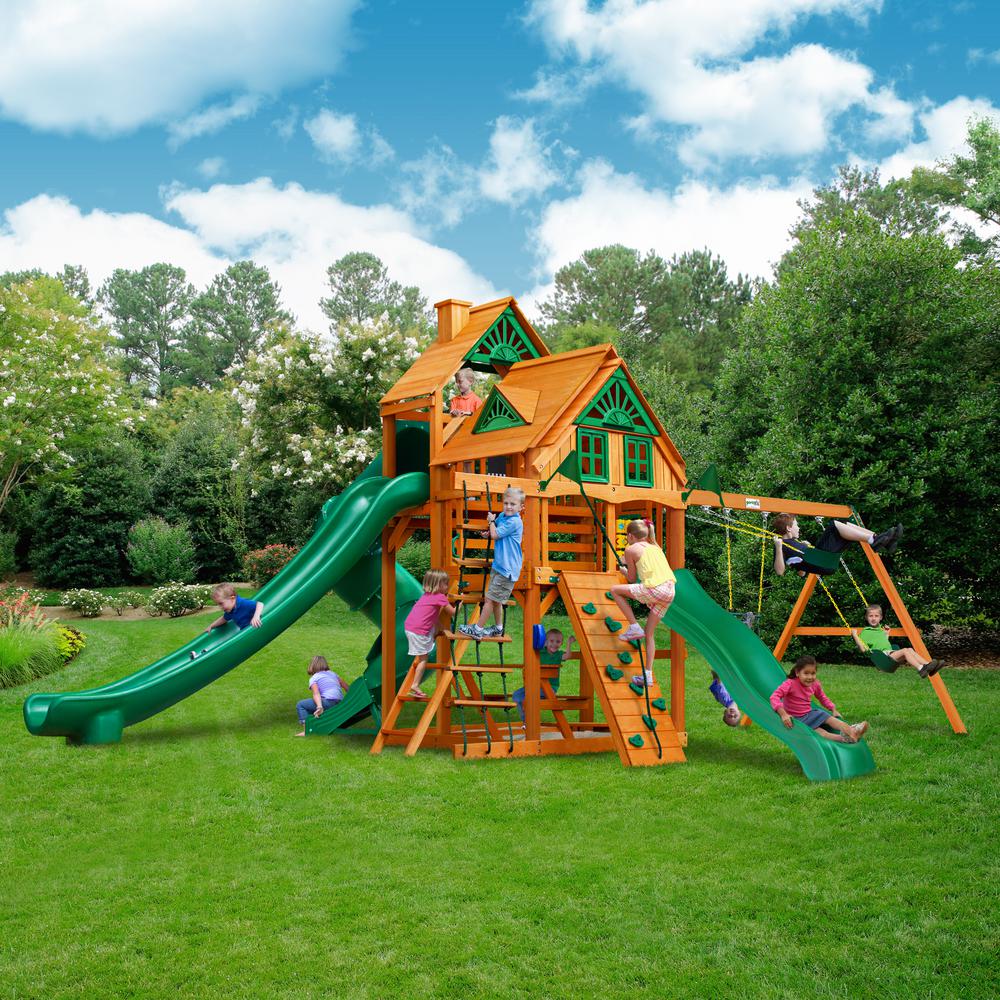 Cedar wooden playset with two green slides, climbing wall, rope ladder, swings, and children playing outdoors