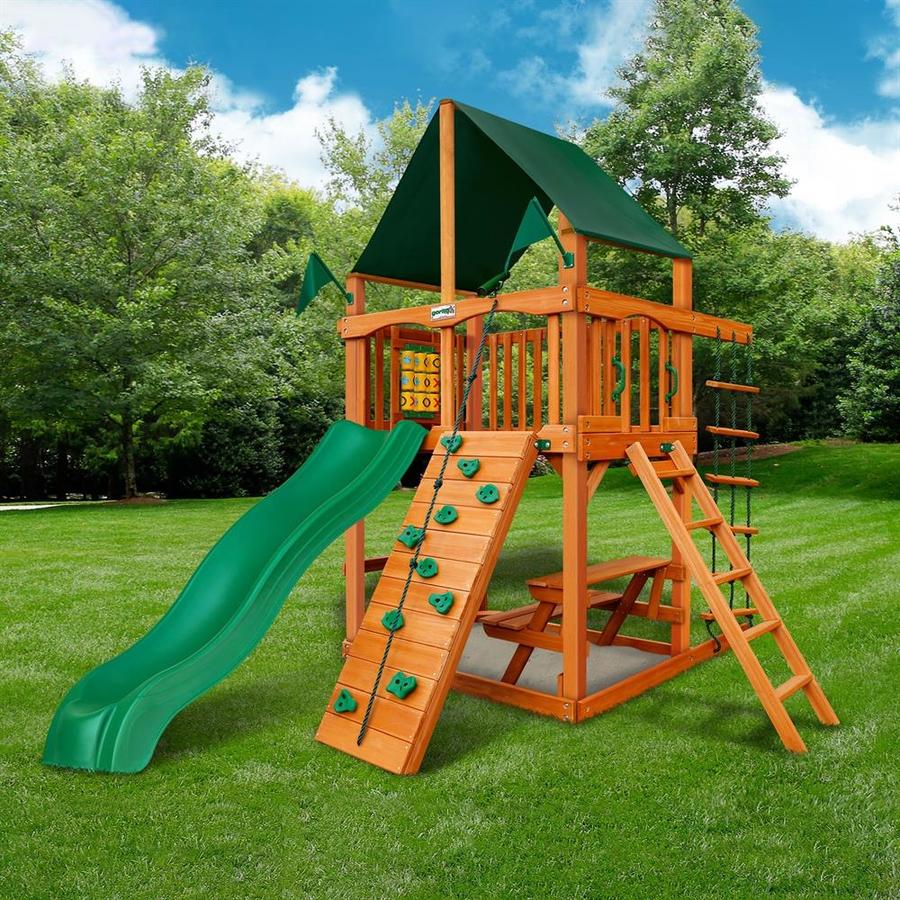 Wooden playset with green slide, rock climbing wall, rope ladder, tic-tac-toe panel, and built-in picnic table on grass