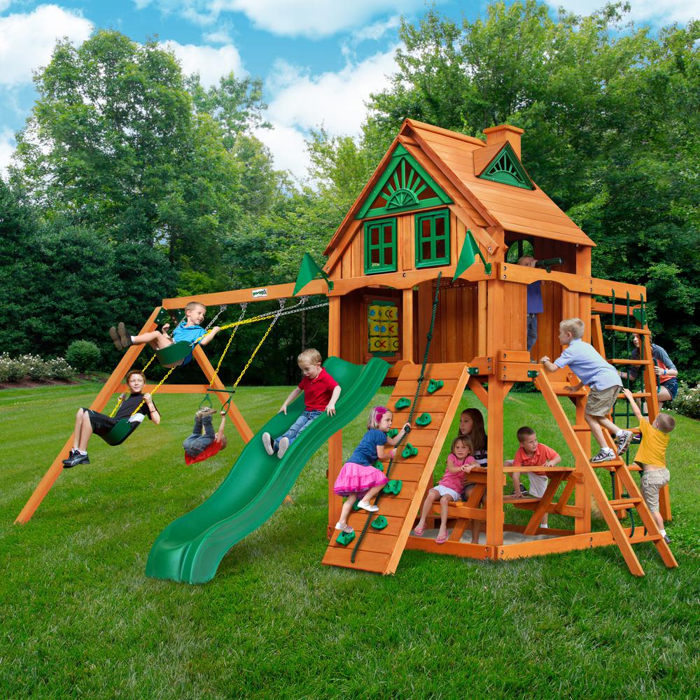 Wooden playset with green slide, swings, climbing wall, picnic table, and tic-tac-toe panel, children playing outdoors