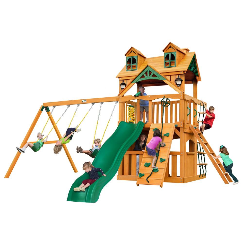 Wooden playset with green slide, swings, climbing wall, rope ladder, and upper clubhouse featuring decorative roof and windows, children playing