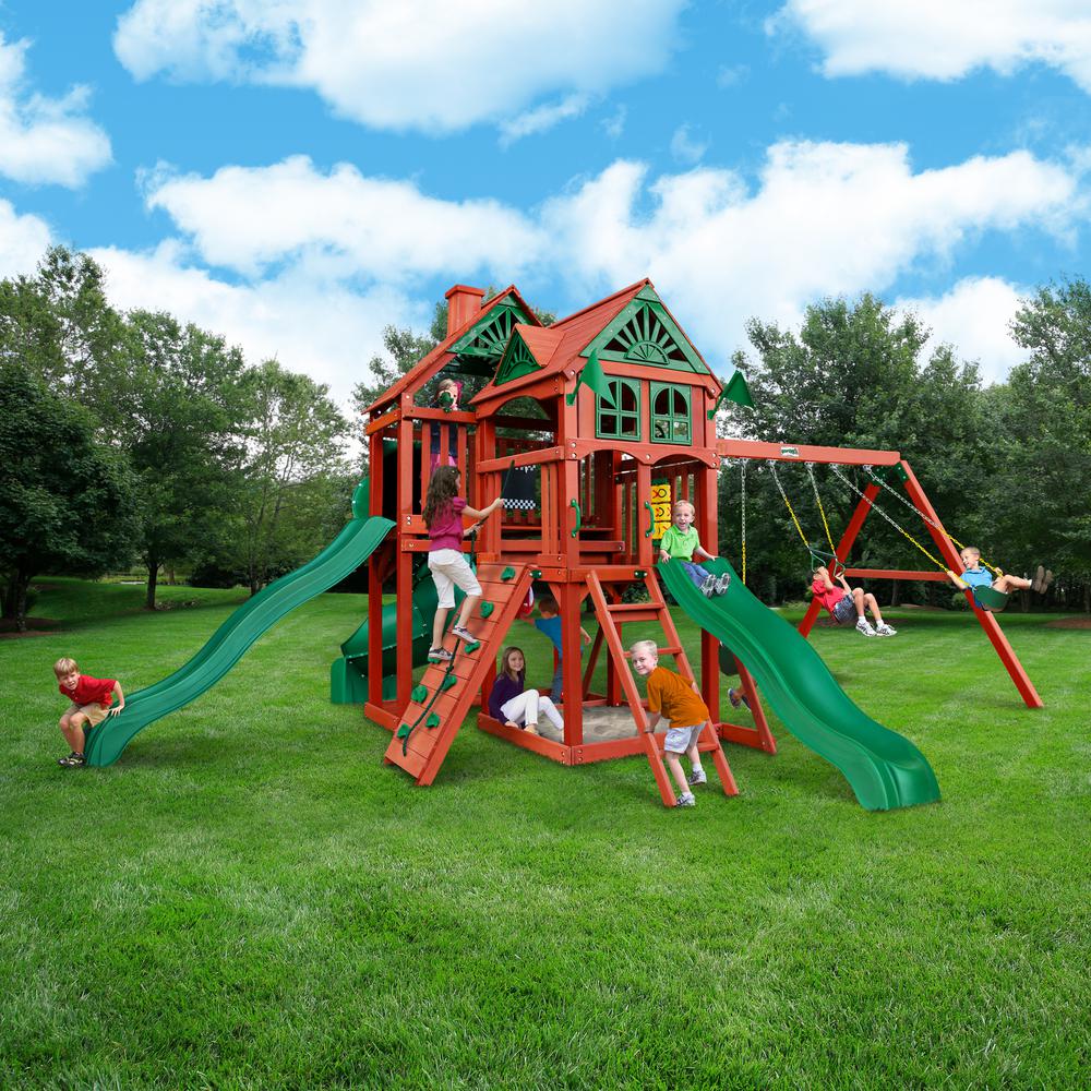 Cedar wooden playset with two slides, swings, climbing wall, sandbox, and playhouse featuring decorative roof and flags