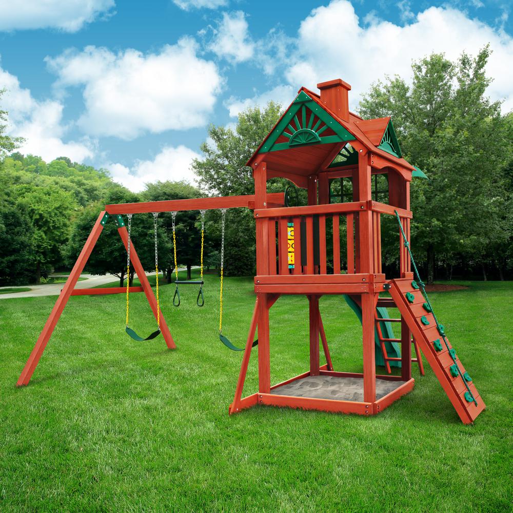 Cedar wooden swing set with clubhouse, rock climbing wall, two belt swings, trapeze bar, slide, and sandbox on green lawn