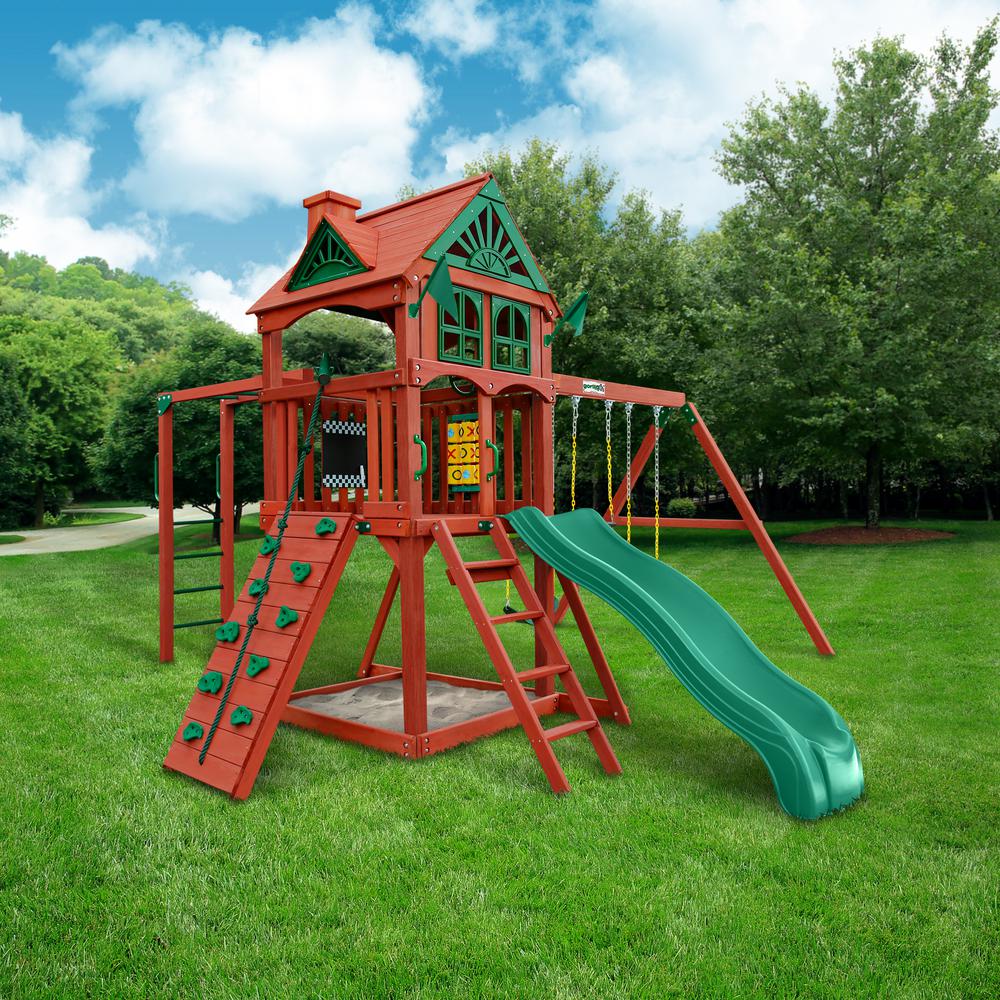 Cedar wood playset with green wave slide, rock climbing wall, two swings, sandbox, and tic-tac-toe panel on grass lawn