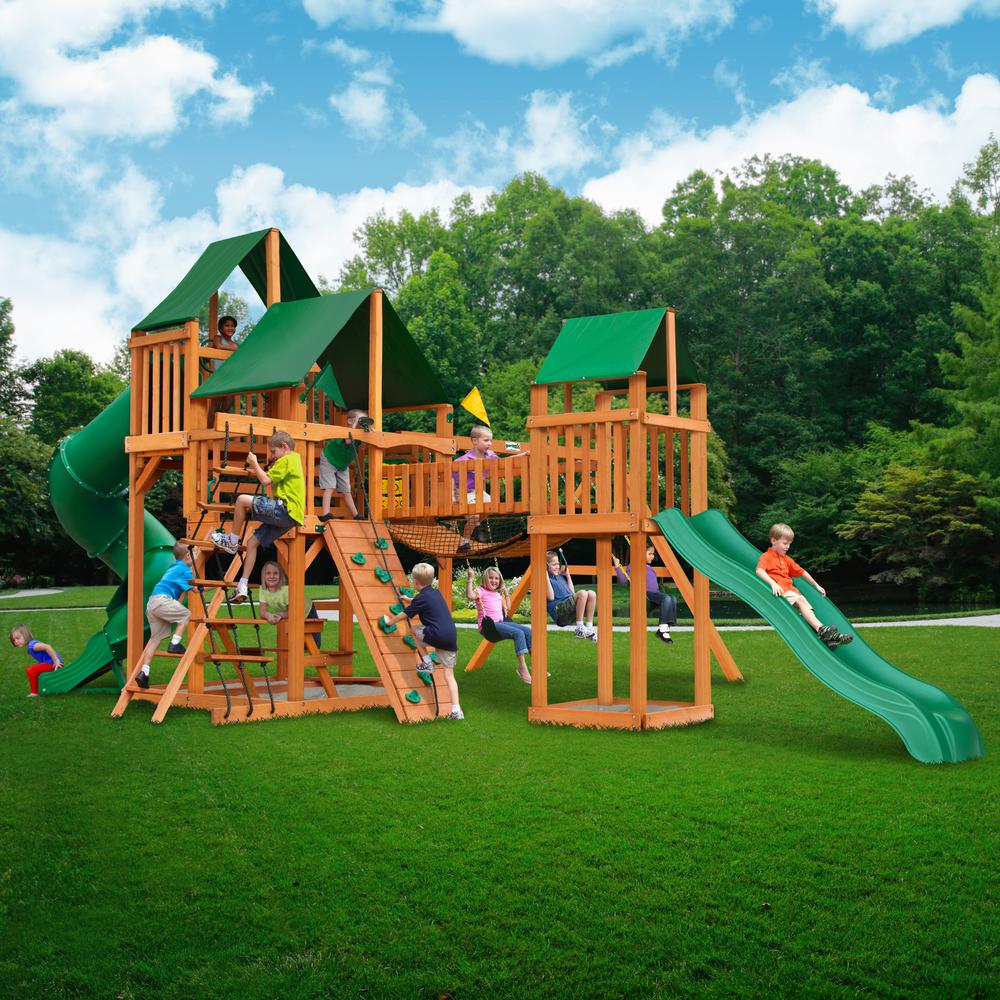 Wooden playset with green vinyl canopies, tube slide, rock wall, climbing ropes, swings, and children playing outdoors