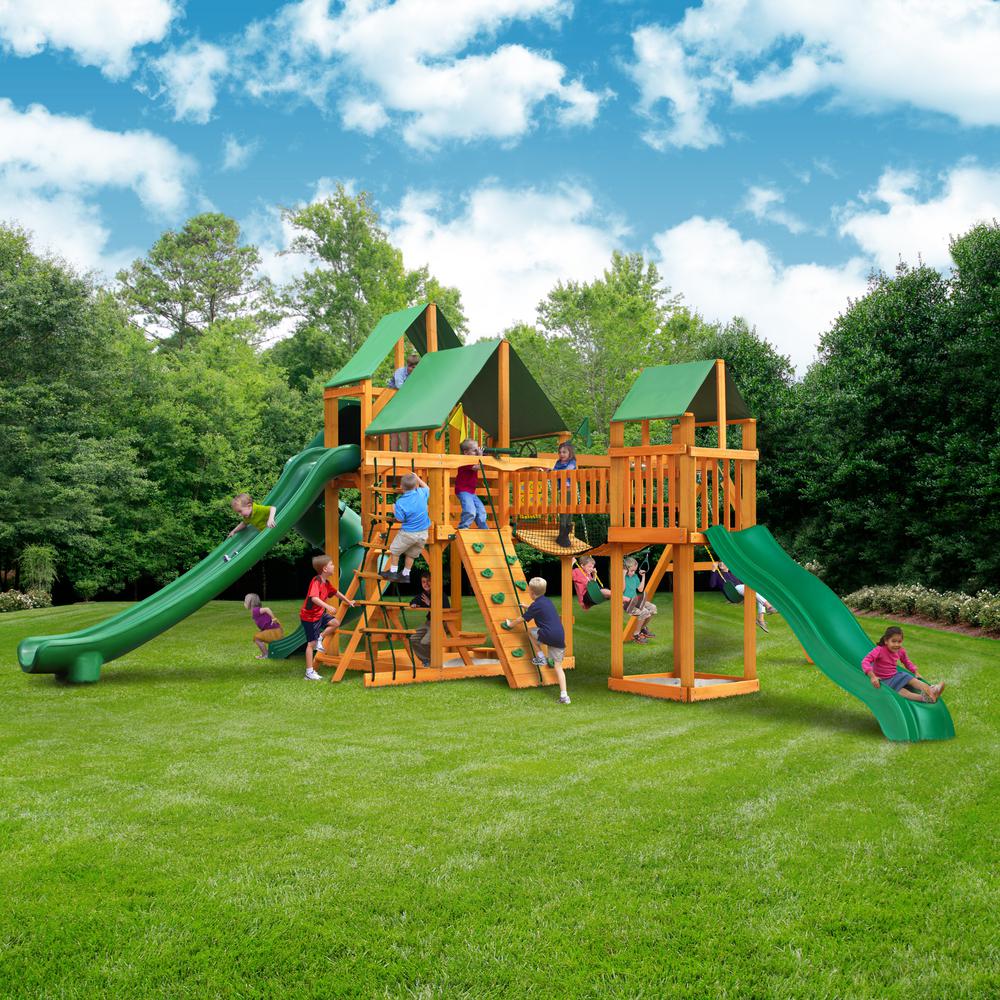 Wooden playset with green vinyl canopy, multiple slides, climbing walls, rope ladders, swings, and children playing on grass
