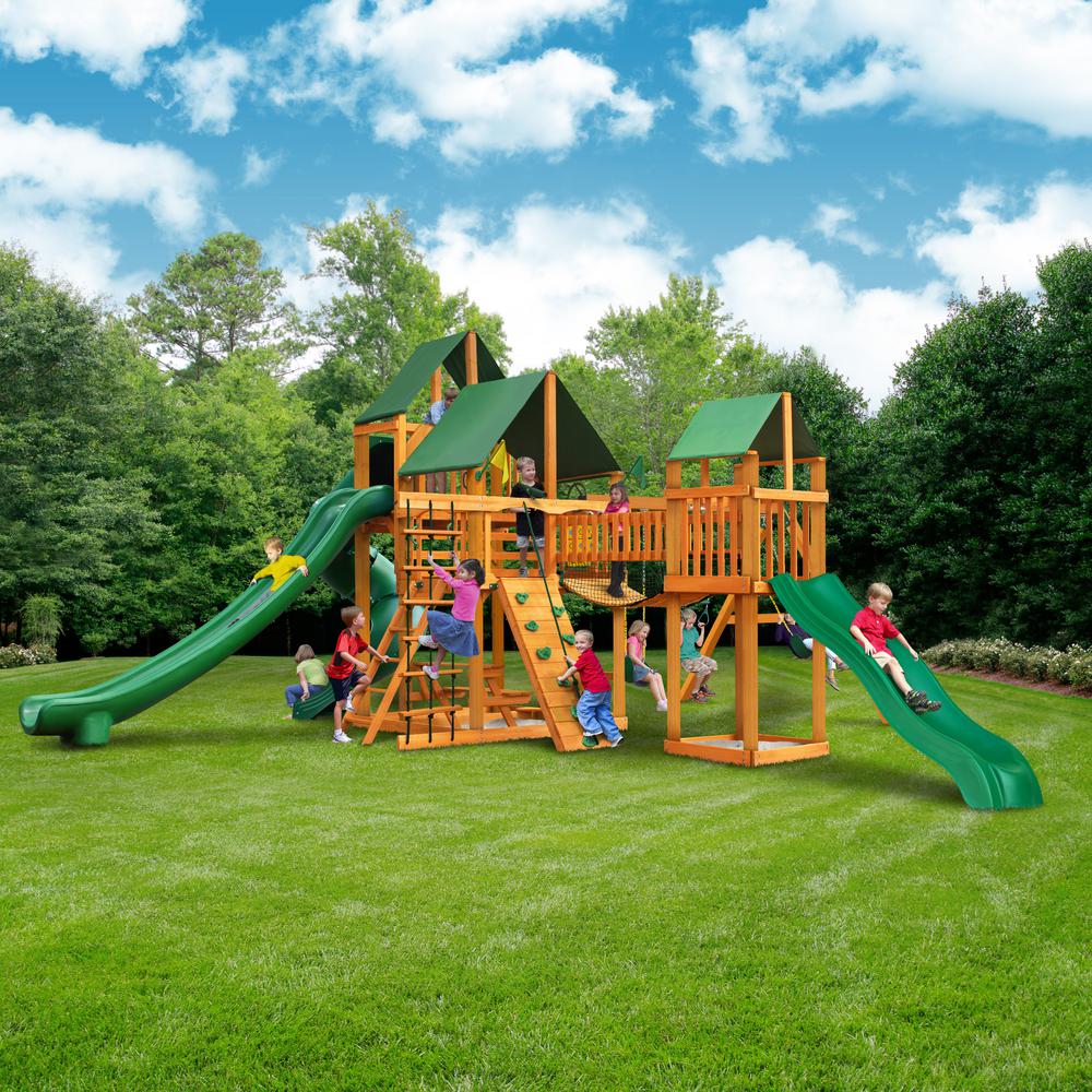 Wooden playset with green canopy roofs, two green slides, climbing wall, rope ladder, swings, and children playing outdoors
