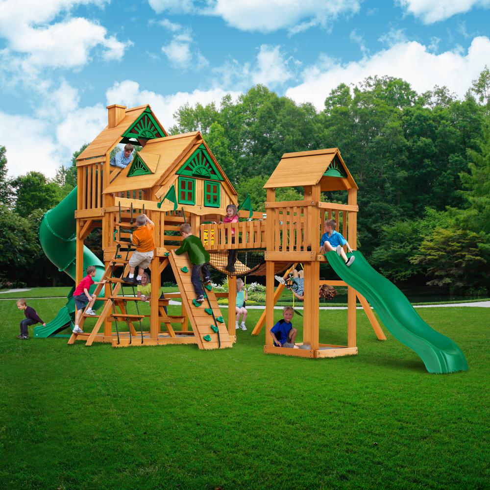 Cedar wooden playset with green slides, climbing walls, rope ladders, multiple towers, and children playing outdoors