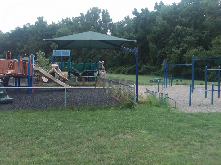 Dark green cantilever square umbrella providing shade over playground slides and climbing structures in a park setting
