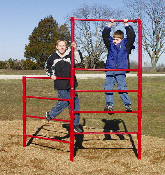 Red metal climbing frame with two children playing on wood chip ground surrounded by trees and grass
