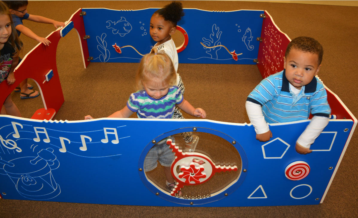 Indoor Tot Corral with colorful panels featuring musical notes, sea creatures, and shapes, surrounded by toddlers on carpeted floor