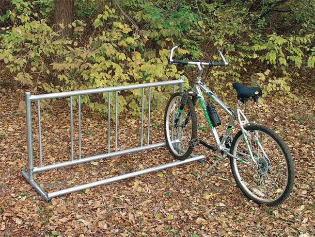 Single Entry Bicycle Rack with silver metal frame holding one bicycle outdoors on leaf-covered ground near green foliage