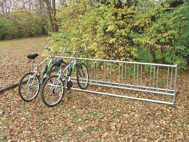 Double Entry Bicycle Rack with two bicycles parked outdoors on fallen leaves near green foliage, durable metal design for secure bike storage.