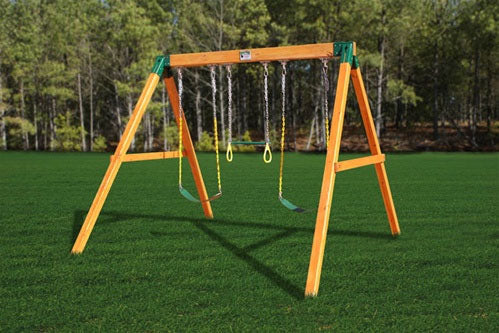Free Standing Three Position Wooden Swing Set with two traditional swings and one trapeze bar on green lawn with trees background