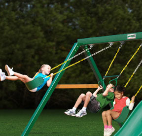 Three children playing on a green swing set with two yellow-chain belt swings and one acrobatic swing bar outdoors