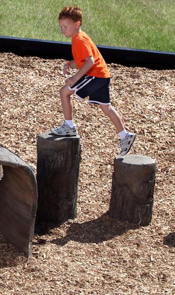 A child climbing on nature-themed tree stump steppers in a playground.