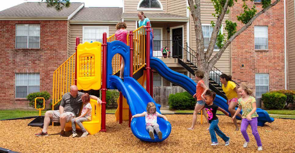Colorful playground with blue wave and curved slides, yellow climbing panels, and children playing on wood chip ground
