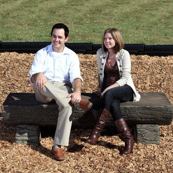 Realistic log bench with wood grain texture and bark finish, sturdy concrete construction, two people seated outdoors on mulch.