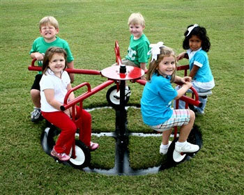 Children playing on a red steel merry-go-round with solid wheels on green grass, promoting outdoor activity and coordination