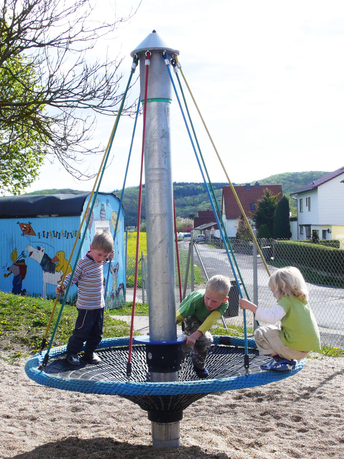 Blue rope bird's nest carousel with steel pole and colorful support ropes in outdoor playground setting
