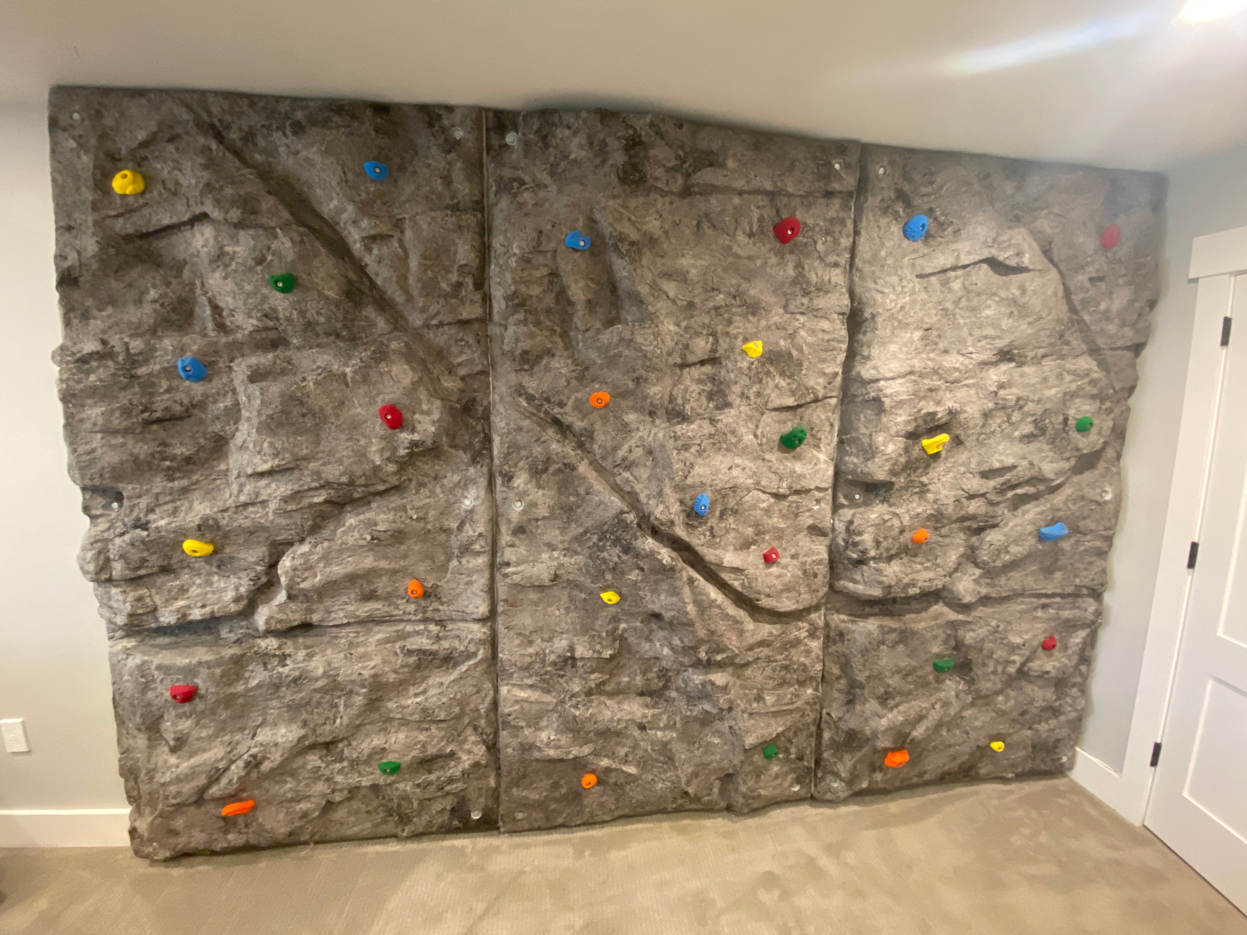 Indoor modular climbing wall with textured gray panels and multicolored climbing holds for versatile play and skill development