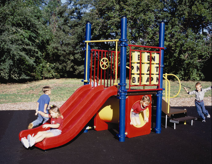 Colorful modular playground with red slides, yellow tunnel, blue posts, and children playing on black safety surface outdoors