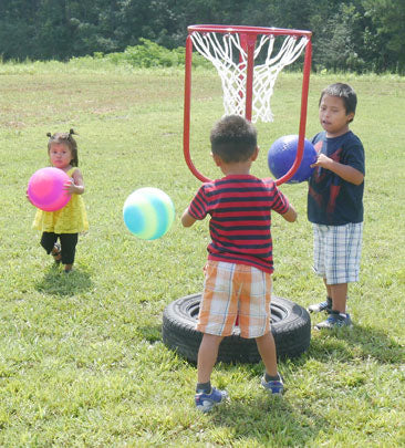 Children playing with colorful balls around a portable basketball hoop with a tire base on grass