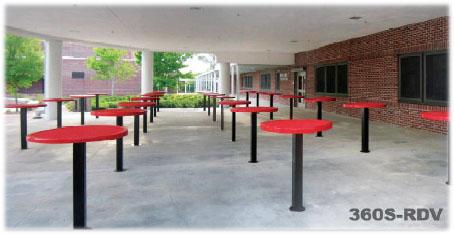 Round outdoor food court tables with solid plank tops and black pedestal bases arranged under a covered dining area