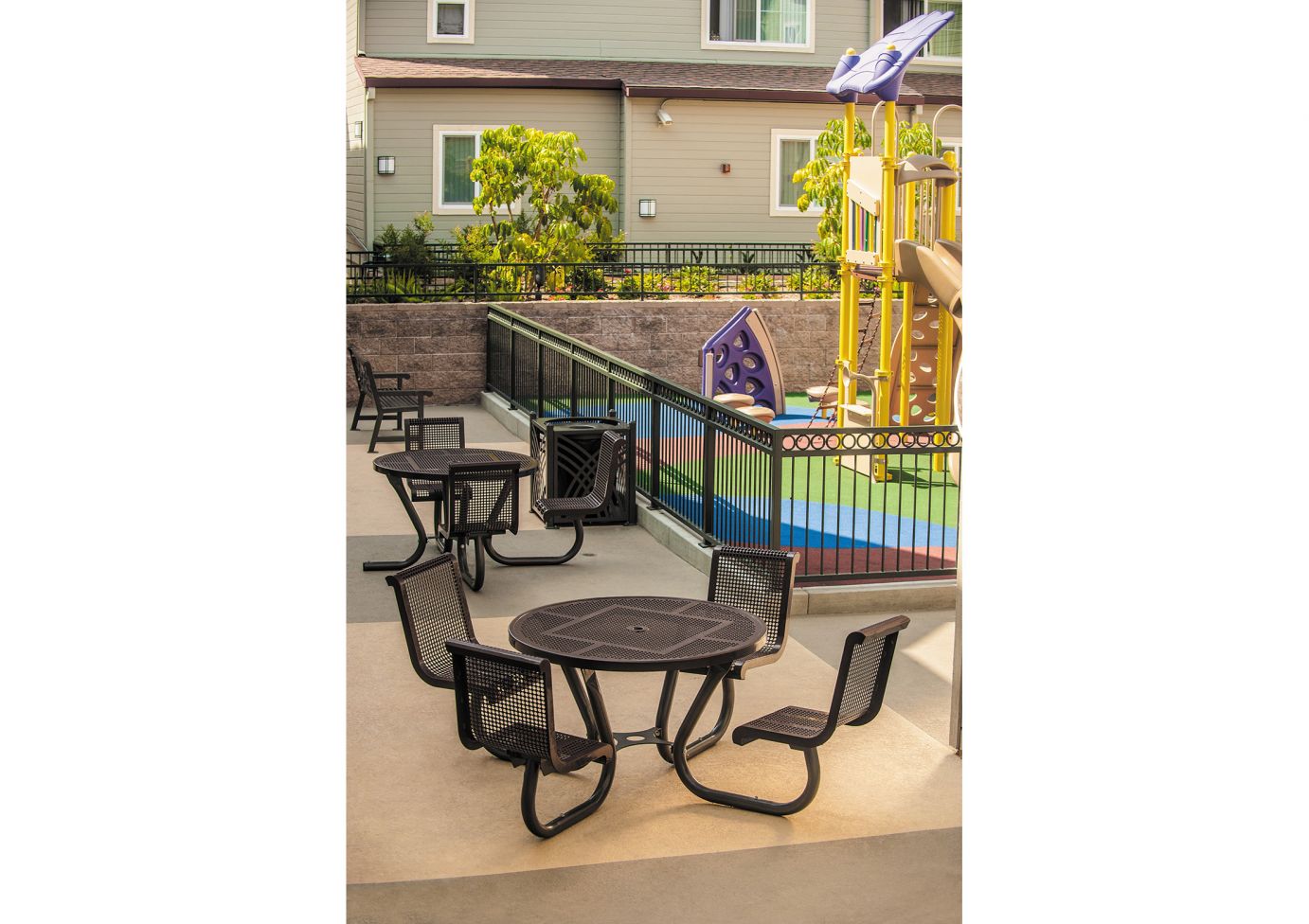 Round black steel picnic table with diamond-patterned top and four contoured mesh seats on outdoor patio near playground