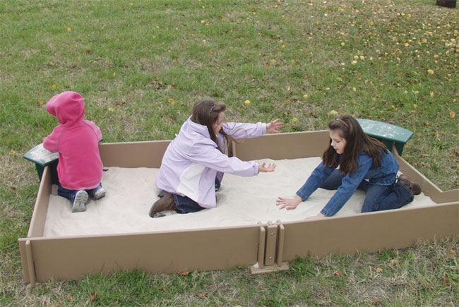 Large outdoor sandbox with three children playing, featuring built-in green seats on surrounding grass.
