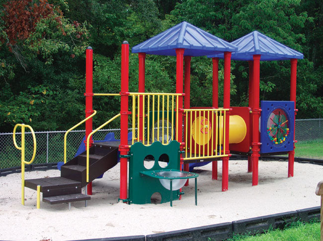 Colorful modular playground with red posts, blue roofs, yellow railings, slides, crawl tunnel, and interactive panels on sand surface