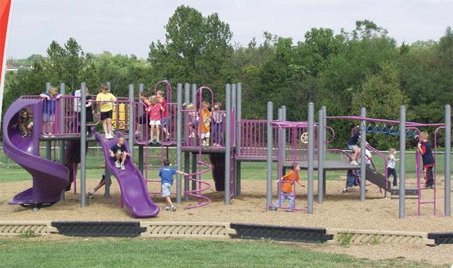 Large purple modular playground with slides, climbing structures, and children playing on woodchip surface outdoors