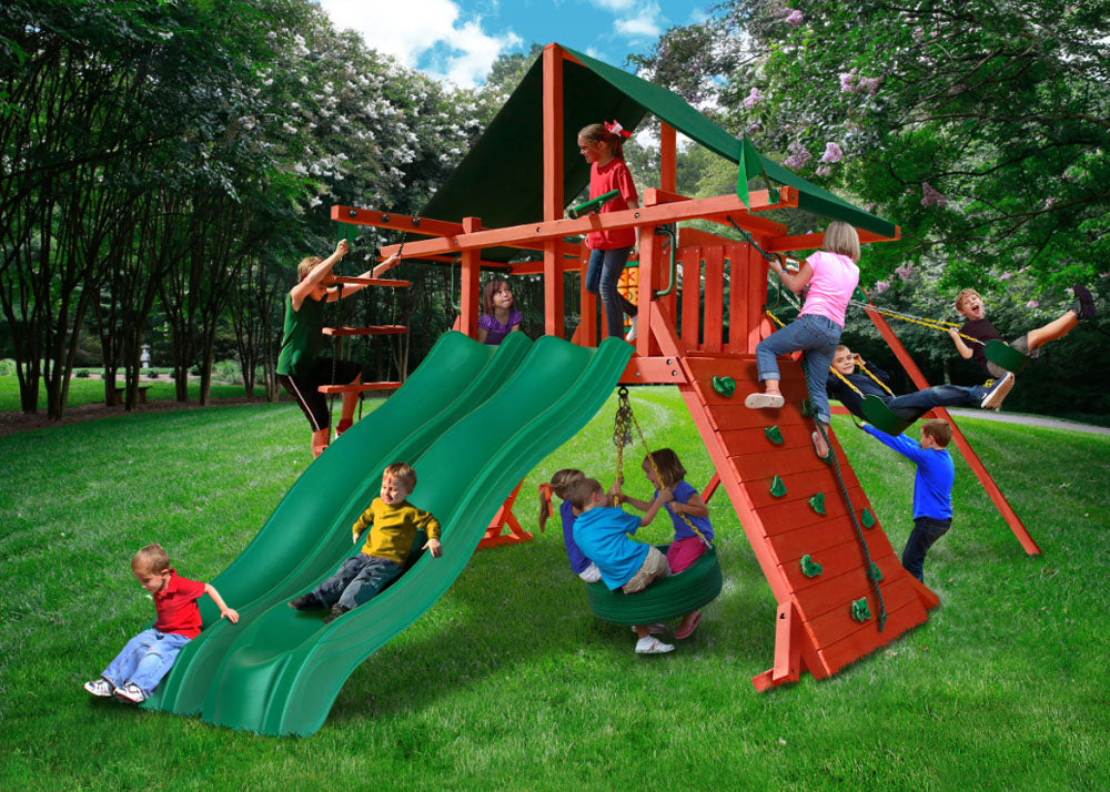 Redwood-finished wooden playset with two green wave slides, climbing wall, swings, tire swing, and green canopy with children playing