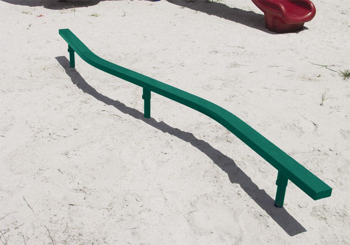 Curved green painted balance beam on sandy playground surface with red playground slide nearby