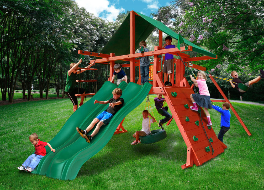 Sun Valley Extreme Wooden Swing Set with dual green Alpine Wave slides, rock climbing wall, tire swing, and green canopy in backyard.